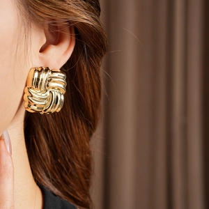 Close-up of a model wearing square woven gold earrings with a polished metallic finish