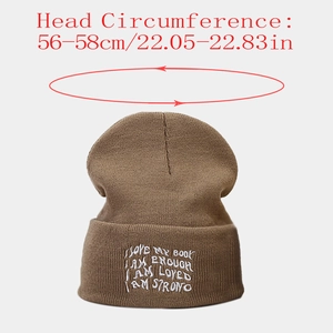 Detail of coffee brown knit beanie featuring white embroidered letter patch and ribbed texture