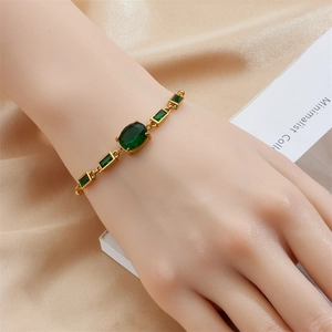 Detail of a vintage gold chain bracelet featuring an oval and square emerald green gemstone