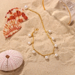 Detail shot of 18K gold plated anklet with white pearl tassels on a beach background