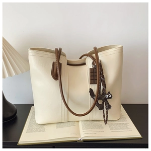 Detail of cream white tote bag with long brown straps and cute charms on a book