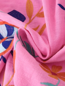 Close-up of pink cotton fabric with colorful floral embroidery on a summer cardigan