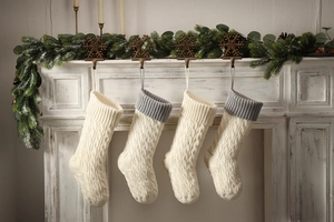 Detail of four cable knit Christmas stockings hanging on a festive white fireplace mantel
