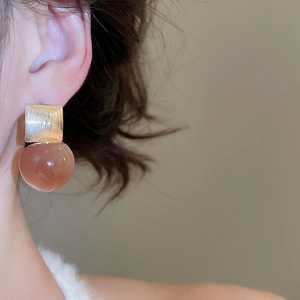 Close-up of gold square metal and amber resin bead drop earring worn by a model