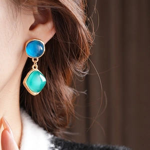 Détail de boucles d'oreilles vintage dorées avec gemmes bleues et vertes sur modèle