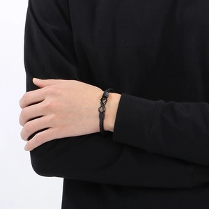 Detail shot of men's black braided leather bracelet featuring a metal infinity charm closure