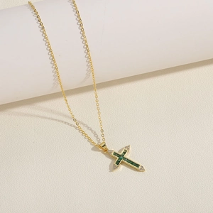 Close-up of 14K gold plated necklace featuring a green zircon cross pendant on a white prop