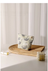 Detail of swan jacquard cosmetic bag with floral metal zipper on wooden tray