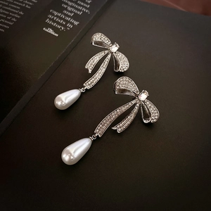 Detail of silver bow earrings featuring sparkling rhinestones and drop imitation pearls