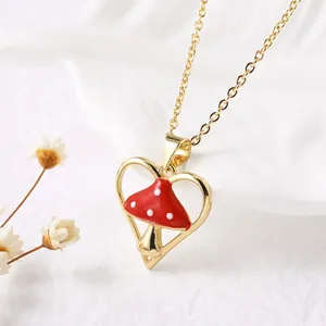 Macro detail of gold heart pendant necklace featuring a red and white enamel mushroom