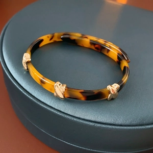 Close-up of tortoise shell resin cuff with golden X cross metal embellishments