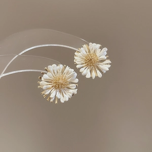 Macro detail of white daisy flower stud earrings with golden center on minimal background