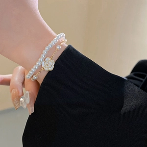 Detail of camellia flower charm and pearl layered bracelet on a model wrist
