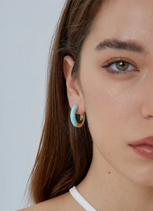 Close-up of elegant C-shaped gold and light blue enamel hoop earrings on a model