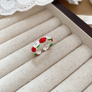 Detail view of silver apple ring with red and green enamel in a beige jewelry box