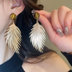 Close-up of elegant gold feather earrings with tiger eye stone worn by a model