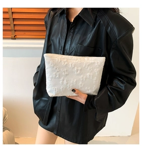 Close-up of white embossed floral pattern on small fabric clutch bag held by model