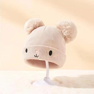 Nahaufnahme einer Baby-Strickmütze mit zwei Bommeln und süßem gesticktem Bärengesicht