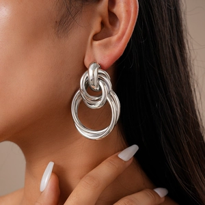 Close-up of interlocking silver-tone geometric knot earrings worn by a model