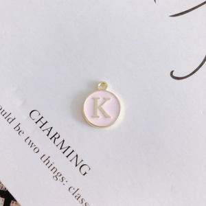 Detailed view of round pink enamel pendant with gold metal letter K for jewelry making