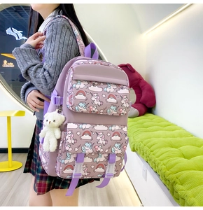 Detail of purple nylon backpack with unicorn rainbow pattern and white teddy bear keychain