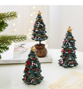 Three miniature green resin Christmas trees with gold stars and red bows on a cozy desk