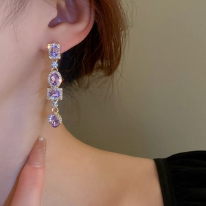 Close-up of elegant gold drop earrings with purple gemstones and crystals on a model