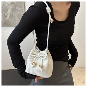 Dettaglio della borsa a secchiello bianca intrecciata con chiusura a coulisse e sfere dorate