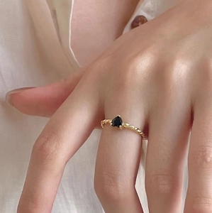 Detail of twisted gold ring band featuring a black heart-shaped zircon on a model's finger