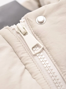 Nahaufnahme der beigen Jacke mit Harzreißverschluss und hochwertigen Metalldruckknöpfen