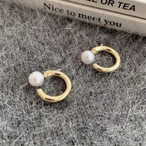 Macro detail of C-shaped gold hoop earrings with white pearls on soft fabric