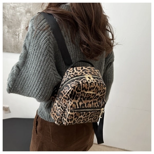 Close-up of leopard print mini backpack showing gold metal zippers and layered pockets