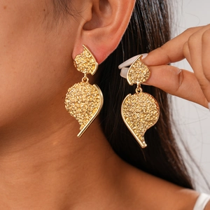 Detail showing the textured metallic gold wrinkled heart earring on model's ear
