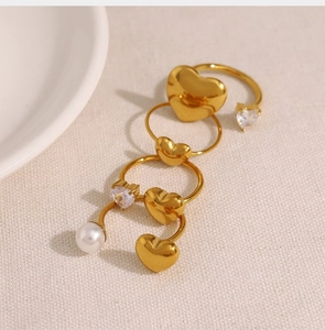 Detailed close-up of golden heart rings with zircon and pearl on textured fabric