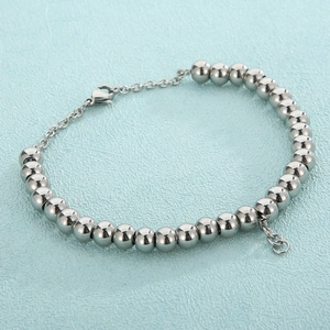 Minimalist stainless steel bead bracelet with lobster clasp on a light blue textured background