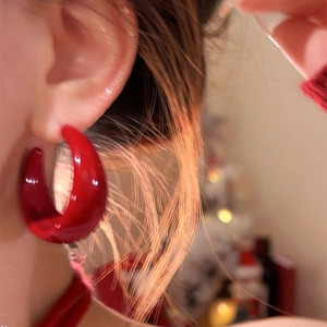 Boucles d'oreilles créoles C en acrylique rouge brillant portées sous lumière chaude