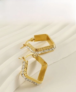 Macro detail of 18K gold plated earrings with zircon pavé and Greek key relief
