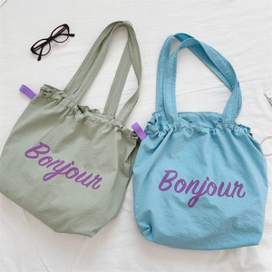 Flat lay of lightweight nylon drawstring tote bags with Bonjour print in green and blue