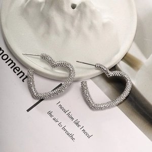 Detailed close-up of heart-shaped silver earrings with textured metallic surface finish