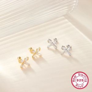 Close-up of gold and silver bow stud earrings with 925 sterling silver certification mark