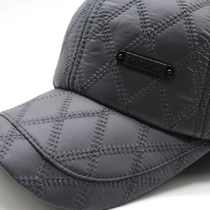 Detail of dark grey winter baseball cap featuring quilted diamond patterns and metal logo