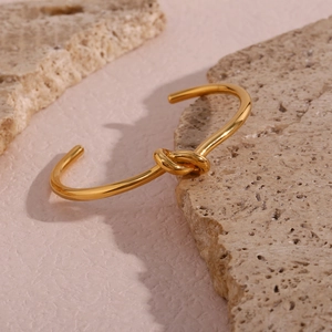 Polished 18K gold-plated stainless steel knotted open bangle on a stone surface