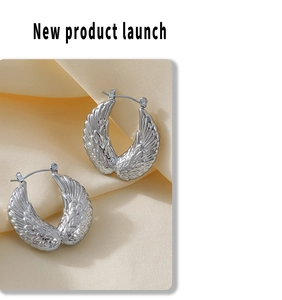 Detailed close-up of silver angel wing earrings with feather texture on beige satin