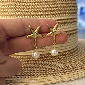 Golden starfish earrings with white pearl pendant held against a summer straw hat