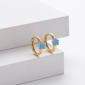 Macro shot of gold hoop earrings with round blue opal insets on a white display stand