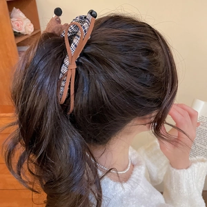 Macro detail of a brown checkered fabric dachshund bow hair clip worn on a side ponytail