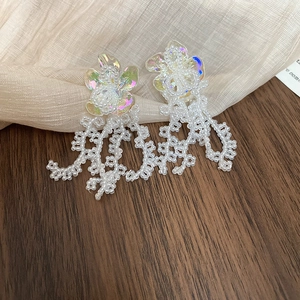 Close-up of iridescent flower earrings with white bead tassels on a textured fabric