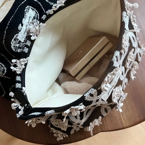 Détail d'une trousse à maquillage en toile noire avec broderie florale blanche et fermeture éclair