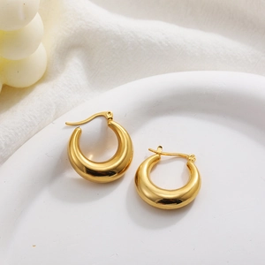 Detailed close-up of chunky gold hollow hoop earrings on a decorative white dish