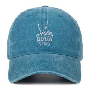 Close-up of white 'GOOD VIBES' embroidery and skull gesture on washed blue baseball cap